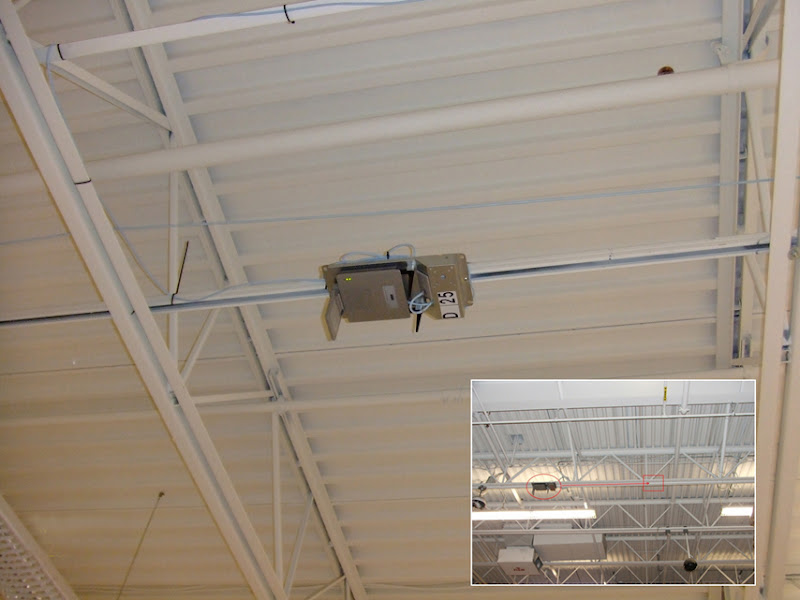 Access point industrial fixado em terça metálica sob a cobertura de um galpão, identificado por etiqueta de infraestrutura e alimentado por PoE via cabeamento estruturado — exemplo de montagem em altura com orientação definida por site survey